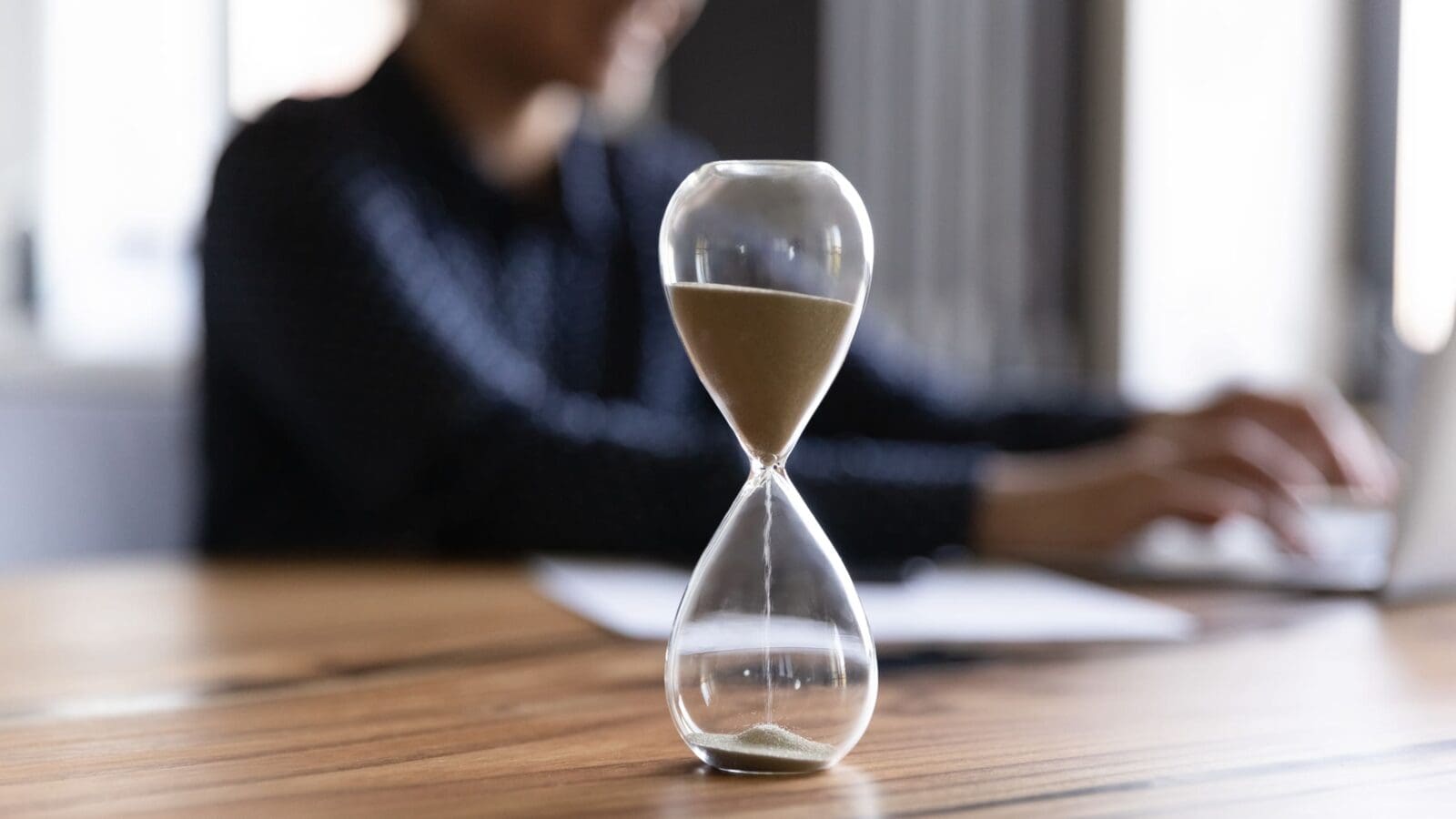 A woman with an hourglass on her desk, making time to measure better. Credit: https://www.istockphoto.com/portfolio/fizkes?mediatype=photography