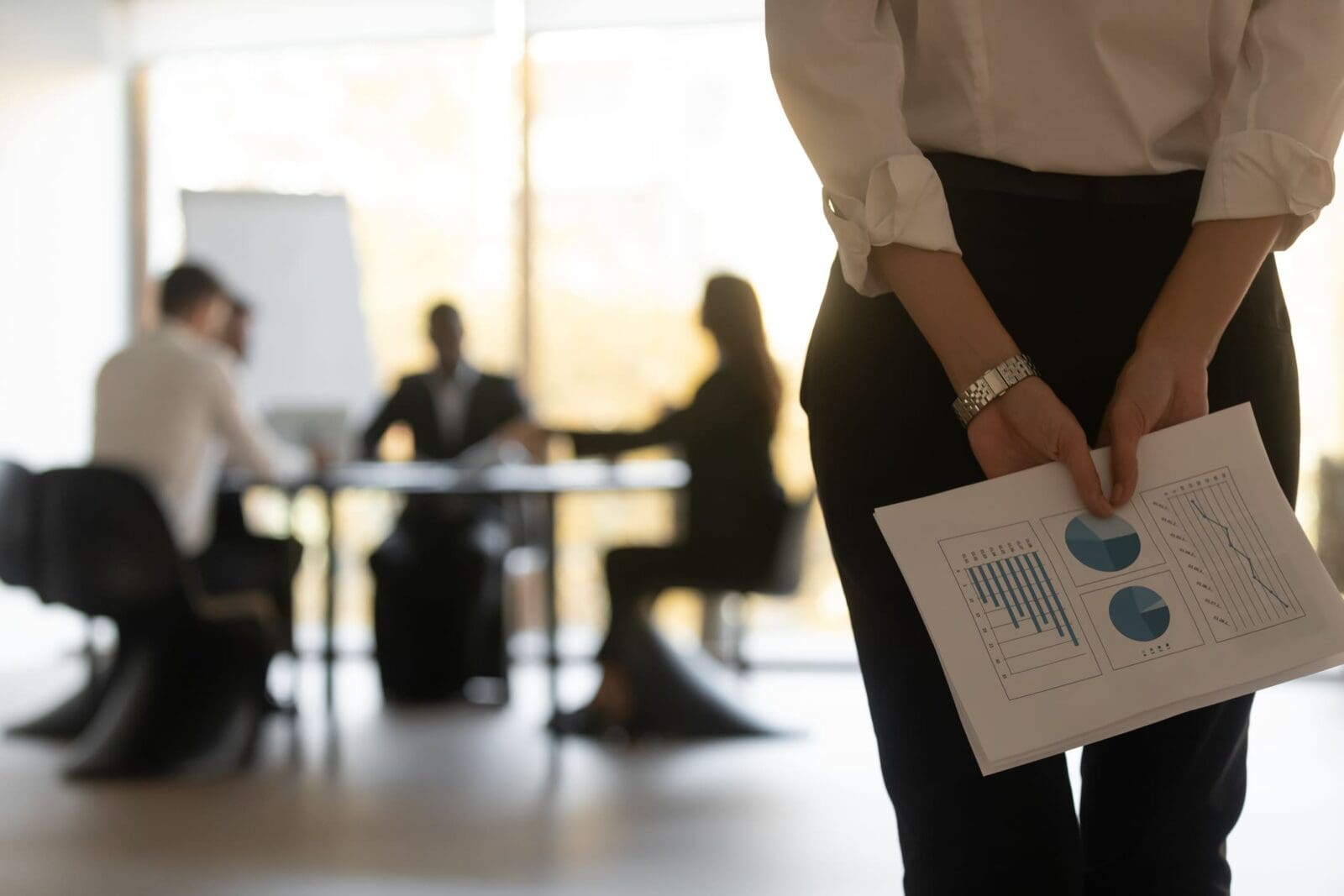 Businesswoman holds KPI report behind her back, not feeling psychological safety. Credit: https://www.istockphoto.com/portfolio/fizkes?mediatype=photography