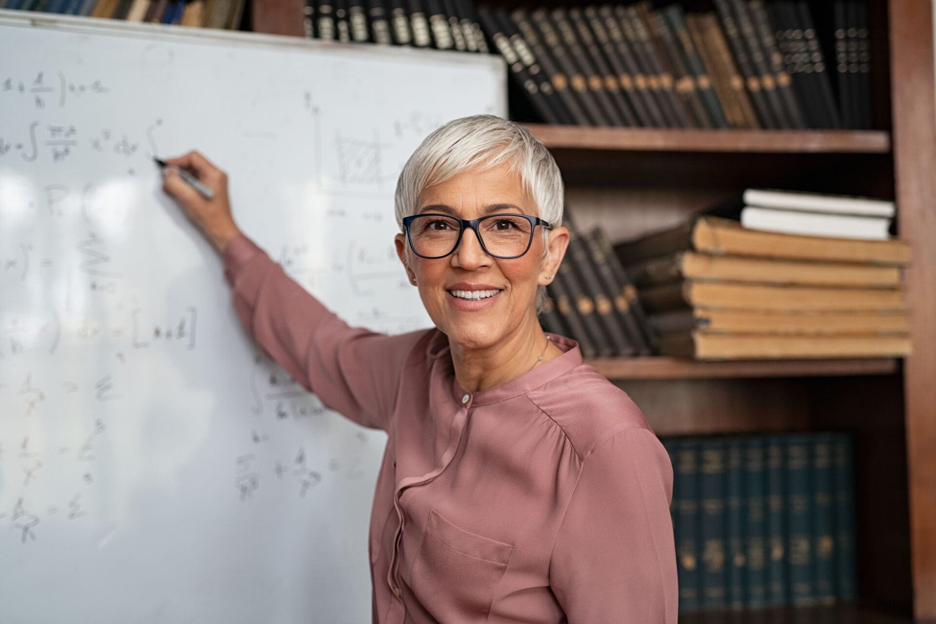 A mature woman writing KPI formulas on a white board. CREDIT: https://www.istockphoto.com/portfolio/Ridofranz