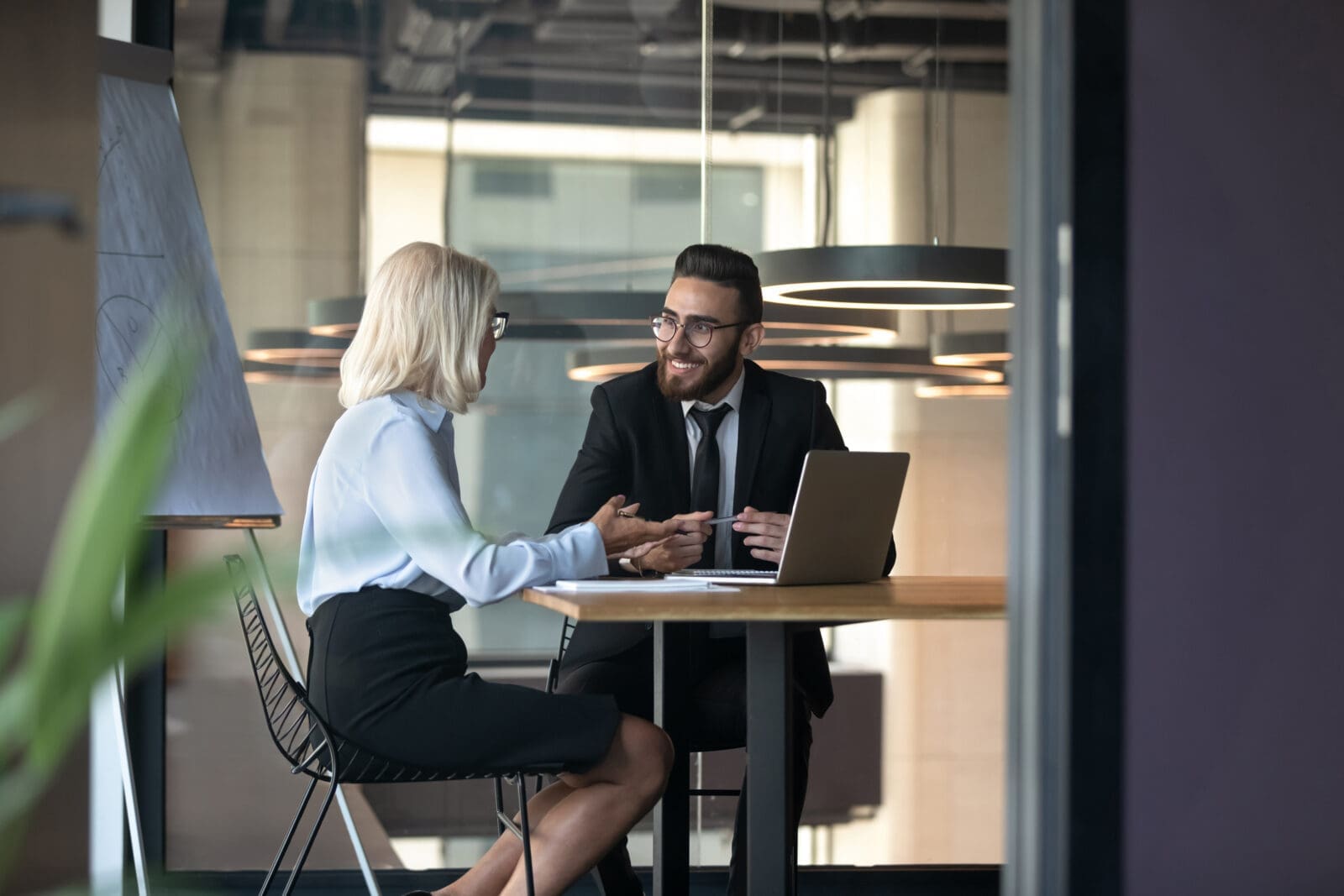 Mature businesswoman and young employee discussing strategy in boardroom with flip chart